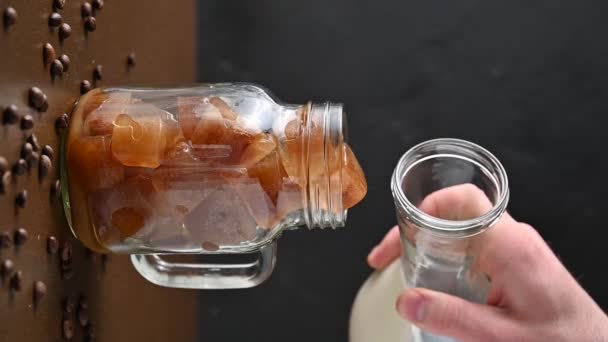 Uma mão de homem derrama leite de uma garrafa em um jarro de gelo de café — Vídeo de Stock