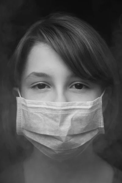 Dark black and white image of a teenager girl in a protective mask surrounded by smoke. — Stock Photo, Image