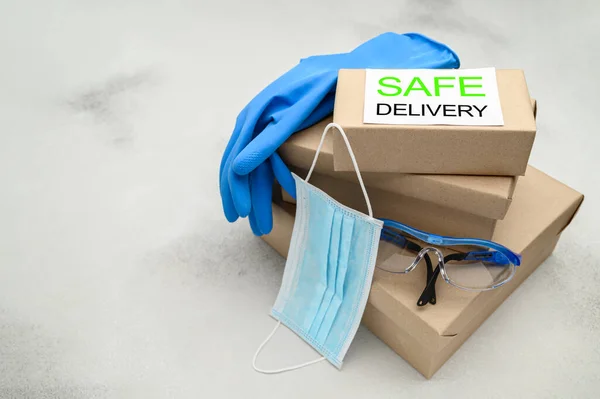 Safe delivery of packages to your home. Cardboard boxes, medical mask, safety glasses and rubber gloves on a white table.