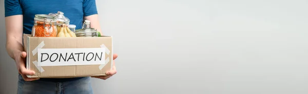 Donation concept. Adult Caucasian male volunteer holds a cardboard box with food on a light background. Voluntary assistance to those in need.