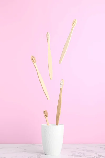 Levitation concept, flying objects. Bamboo toothbrushes fly over a white mug on a pastel pink background.