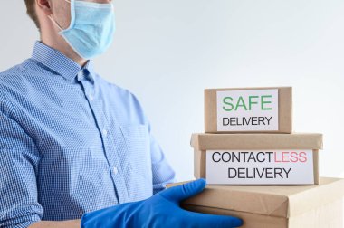 Koruyucu tıbbi maskeli ve eldivenli bir kurye karton kutular ve paketler tutuyor..