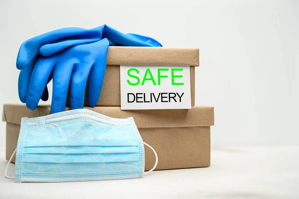 Safe delivery of packages to your home. Cardboard boxes, medical mask and rubber gloves on a white table.