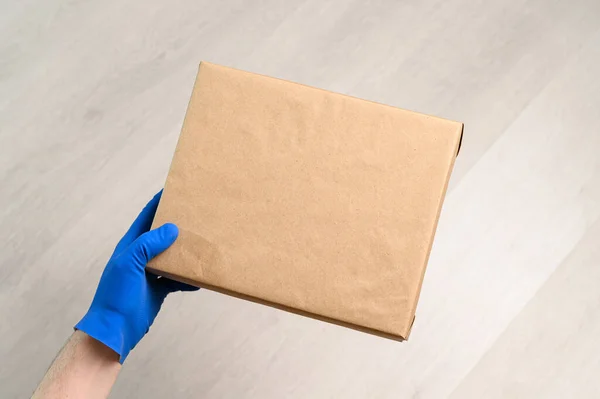 Couriers hand in rubber glove holds cardboard parcel box — Stock Photo, Image