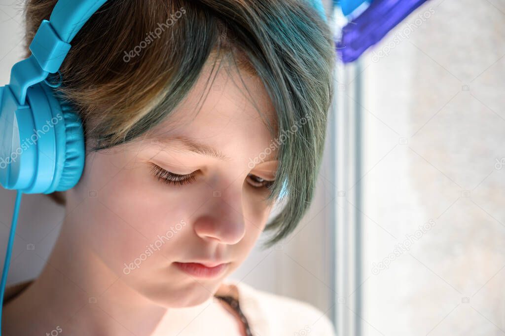 Sad teenage girl in headphones listening to music, leaning on the window. Misses her friends.