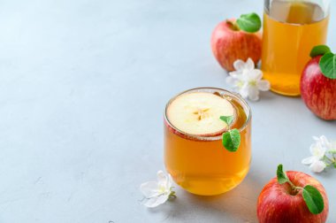 Ev yapımı mayalanmış kombu çayı ya da açık gri bir masa üzerinde bir dilim taze elmayla bardakta elma şarabı..