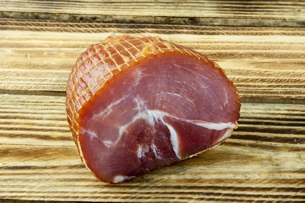 Smoked boneless pork ham hock wrapped in netting on a wooden background — Stock Photo, Image