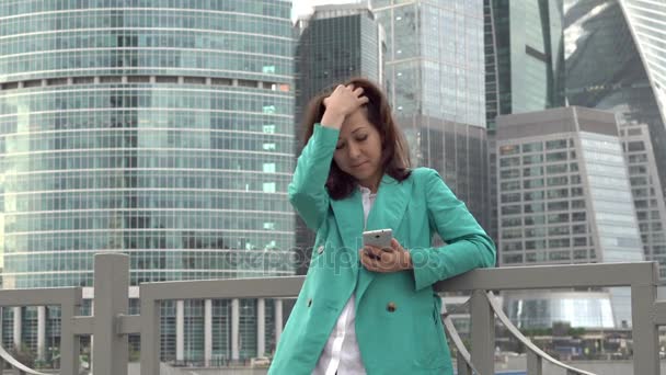 30s woman stands near skyscrapers and using app — Stock Video