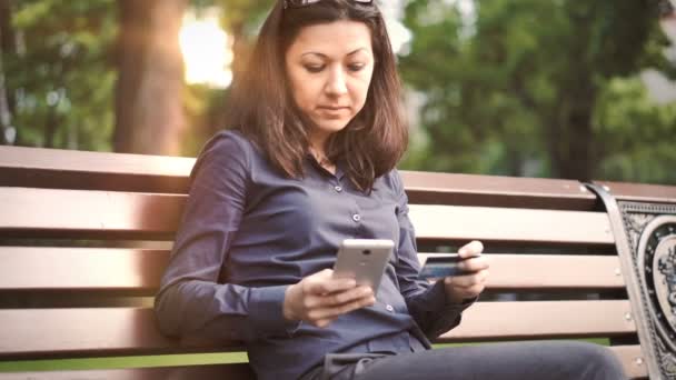 Mujer sentada en el banco hace pagos en línea — Vídeos de Stock