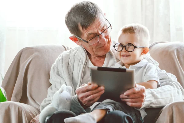 El abuelo mayor y su nieto pequeño usan un dispositivo de tableta. — Foto de Stock