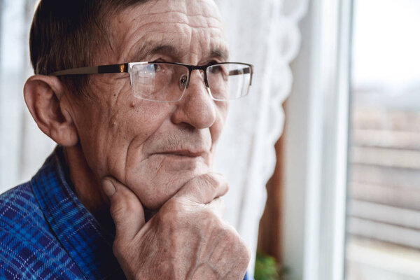 Senior standing at the window and thinking about something or fo