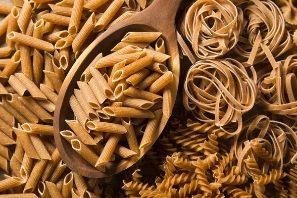 Penne integral en una cuchara. Pastas integrales sobre una mesa de madera — Foto de Stock