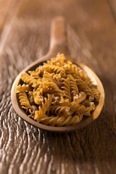 Fusilli integral en una cuchara. Pasta integral sobre una lengüeta de madera — Foto de Stock