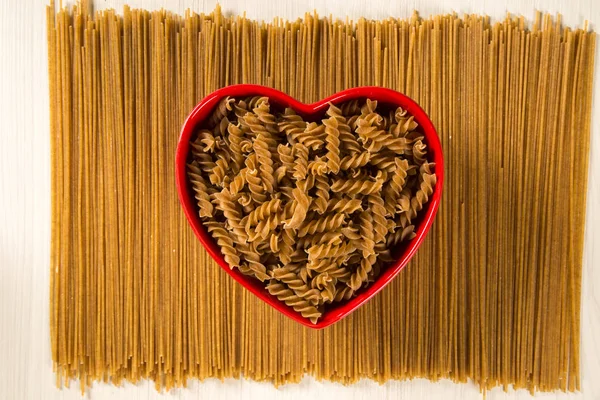 Pastas integrales. Fusilli integral en un tazón de corazón sobre un bosque — Foto de Stock