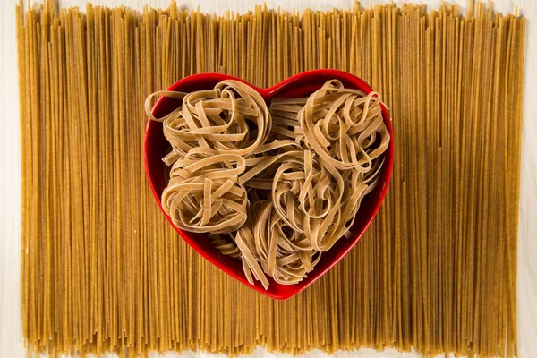 Wholemeal Pasta. Integral tagliatelle into a heart bowl over a w — Stock Photo, Image