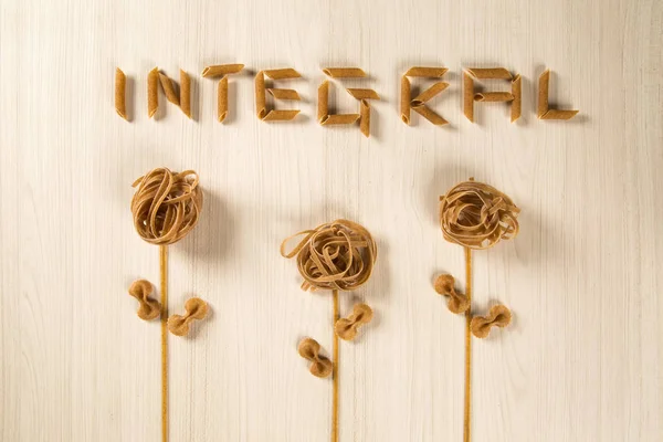 Whole-shaped integral pasta with flowers on a white wooden table
