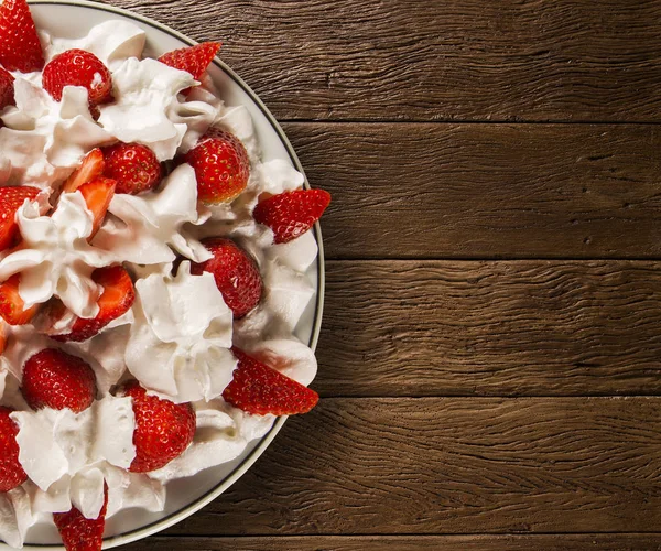 Fragola con crema chantilly in un piatto su un tavolo di legno — Foto Stock