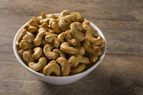 Cashew nuts in white bowl on wood background — Stock Photo, Image
