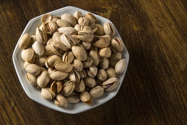 Pistachio nuts in white bowl with wood background. Stock Photo