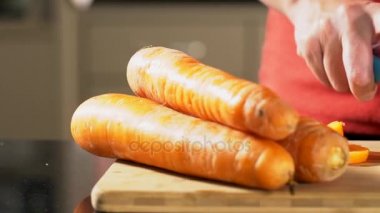 Ev bir mutfak ahşap doğrama tahtası üzerinde bir bıçakla bir havuç eller bir kadının bir bıçak ile kesmek. 