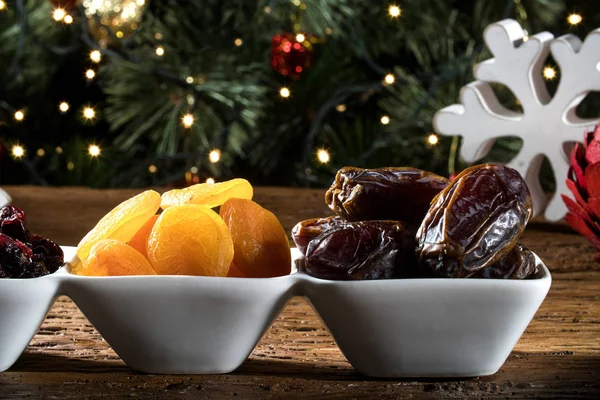 Dried apricots and pitted in a bowl on the board with blurred christmas background. — Stock Photo, Image