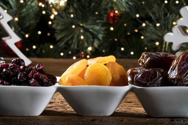 Getrocknete Aprikosen, entsteinte und getrocknete Beeren in einer Schüssel auf dem Brett mit unscharfem Weihnachtshintergrund. — Stockfoto