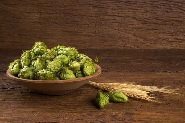 Cerveja ingredientes Cones de lúpulo em tigela de madeira e orelhas de trigo no fundo de madeira . — Fotografia de Stock