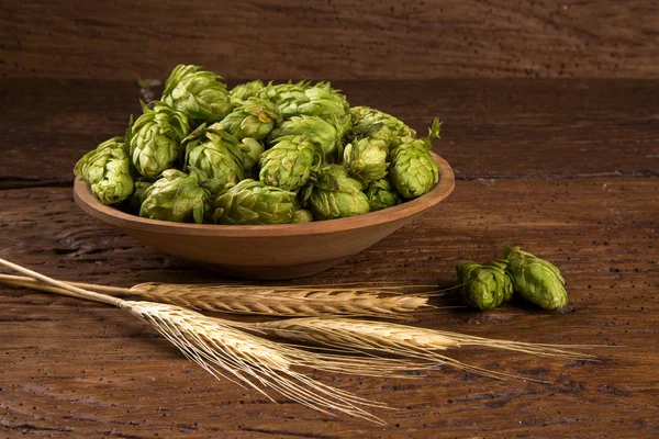 Beer brewing ingredients Hop cones in wooden bowl and wheat ears on wooden background.