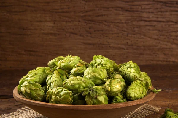 Ingrédients de la bière Cônes de houblon dans un bol en bois et épis de blé sur fond en bois . — Photo