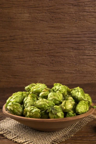 Beer brewing ingredients Hop cones in wooden bowl and wheat ears on wooden background.