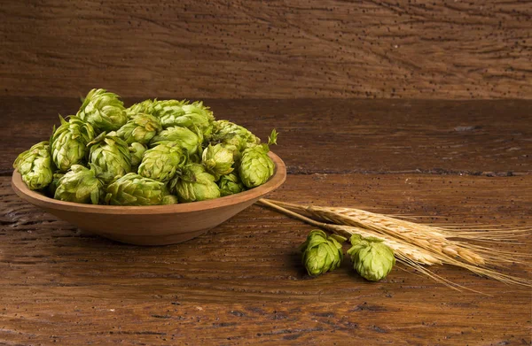Beer brewing ingredients Hop cones in wooden bowl and wheat ears on wooden background. Beer brewery concept