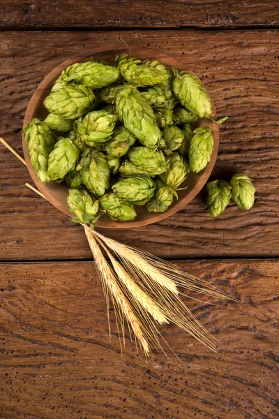 Bierbrauzutaten Hopfenzapfen in Holzschale und Weizenähren auf Holzgrund. Brauereikonzept — Stockfoto