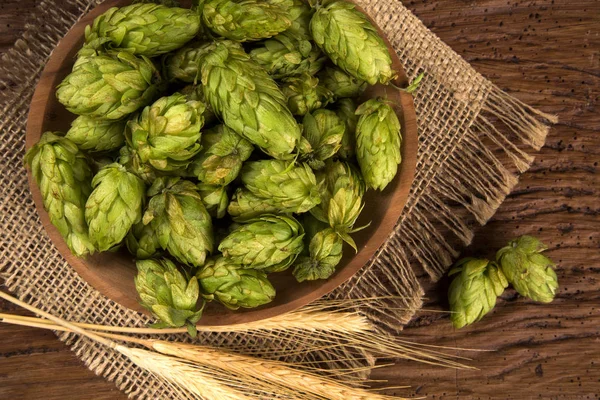 Bierbrauzutaten Hopfenzapfen in Holzschale und Weizenähren auf Holzgrund. Brauereikonzept — Stockfoto