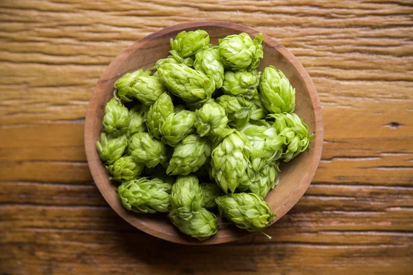 Bierbrauzutaten Hopfenzapfen in Holzschale und Weizenähren auf Holzgrund. Brauereikonzept — Stockfoto