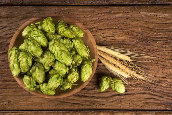 Ingredientes cervejeiros Cones de lúpulo em tigela de madeira e orelhas de trigo em fundo de madeira. Conceito de cervejaria de cerveja — Fotografia de Stock