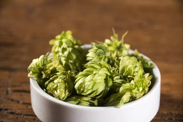 Bierbrauzutaten Hopfenzapfen in Holzschale und Weizenähren auf Holzgrund. Brauereikonzept — Stockfoto