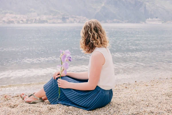 Romantische Frau sitzt am Strand mit Blume — Stockfoto