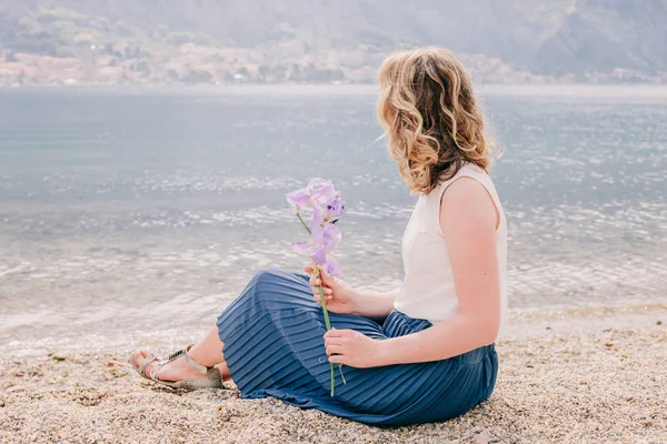 Ρομαντική γυναίκα καθίσει στην παραλία με λουλούδι — Φωτογραφία Αρχείου