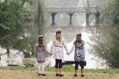 üç küçük kız Göl Manzaralı Parkta yürümek. Kız kardeş