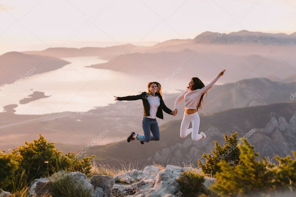 two girls jump and travel in mountains at sunset with beautiful view. Picturesque landscape background.