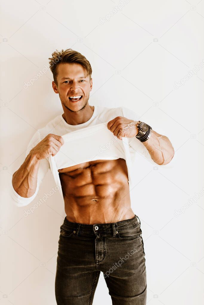 Handsome athletic man wearing white t-shirt. Muscles and abs. Joyful male showing abs stomach