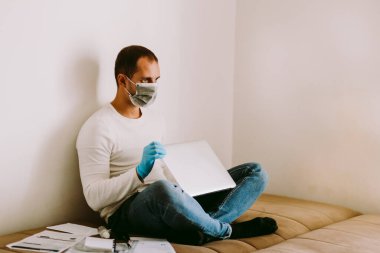 Evde karantina sırasında dizüstü bilgisayarı ve akıllı telefonu olan bir adam. SELF-ISOLATION adamı kavramı Coronavirus COVID-19 sırasında evde çalışıyor..
