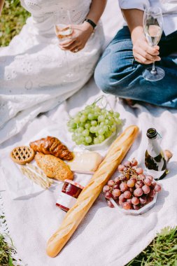 Çift piknikte dışarıda kahvaltı yapıyor. Fransız kahvaltısı kruvasan, reçel, açık havada şampanya..