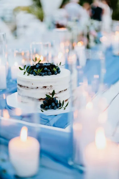 wedding cake with blueberry and blackberry. Elegant fine art wedding photo. Candles lit around. Wedding party setting table coverage. Rustic style with sky blue colour.