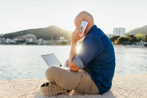 Adam Telefonda Konuşuyor Gün Batımında Deniz Kenarındaki Sahilde Dizüstü Bilgisayar — Stok fotoğraf