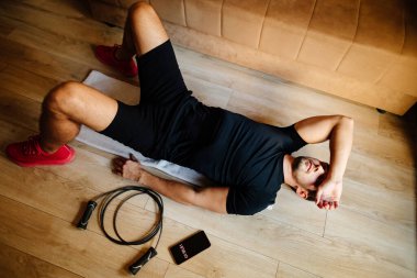 Yetişkin adam spor yaptıktan sonra rahatlar. Erkek spor salonunda yerde yattıktan sonra yorgun düşer. Aşırı eğitim sendromu yorgunluğu