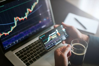 Yatırım borsacısı dizüstü bilgisayar ve telefon kullanarak bitcoin fiyat hareketini tahmin ediyor. Kristal tüccar finansal yöneticisi hisse senedi grafiğini analiz ediyor. Yönetici birden fazla aygıt ve kahve kullanıyor..