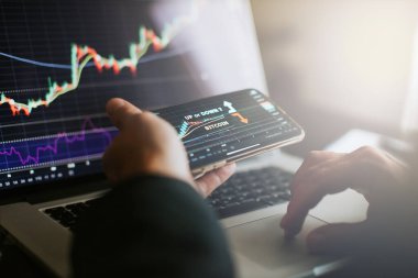 Stocktrader karlı fırsatları analiz ediyor. Bitcoin yatırıyor. İçerde telefon ve laptop kullanan kripto tüccarı..