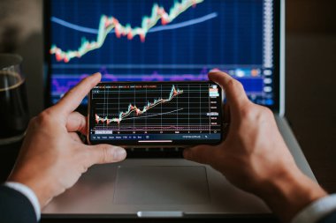 Yatırım borsacısı risk analizi grafiği telefon ekranında. Hisse fiyatları tahmininde birden fazla aygıt kullanan tüccar.