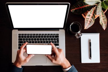 Dizüstü bilgisayar ve telefon düzeni kalem planlama defteri ve telefon ekranı tutan bir iş adamı. Ofis iş yeri, beyaz ekran arka planı. Beyaz ekranlı telefonu tutan adam..